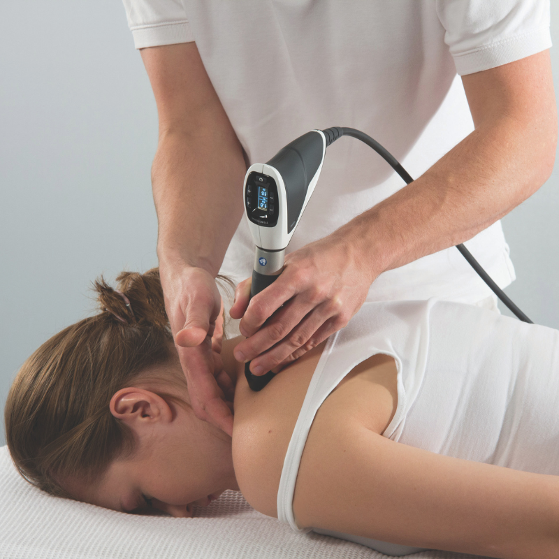 Physiotherapist performing shockwave therapy on a patient’s neck and upper back to treat muscle pain.