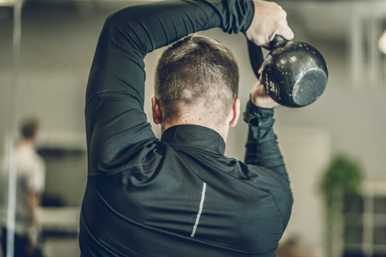 Man performing overhead kettlebell exercise to improve shoulder strength and mobility