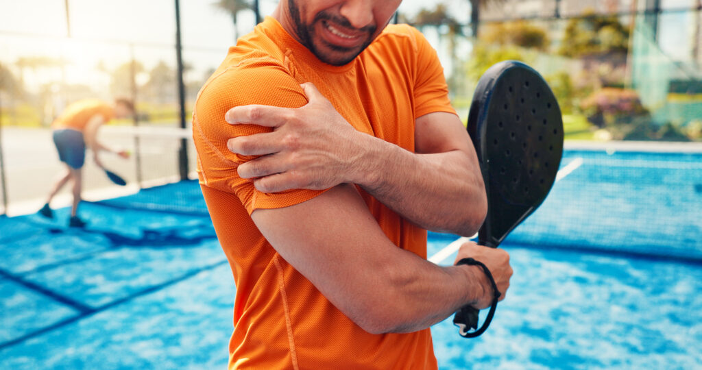 Man holding his painful shoulder while playing padel on a court.